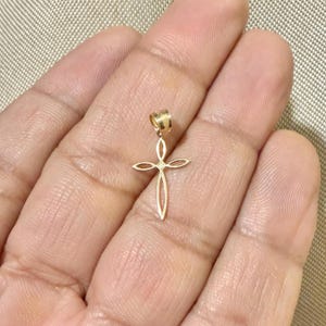 Puede incluir: Un colgante dorado con forma de cruz. La cruz tiene un dise&ntilde;o calado con un peque&ntilde;o detalle en forma de diamante en el centro. El colgante cuelga de un peque&ntilde;o lazo.