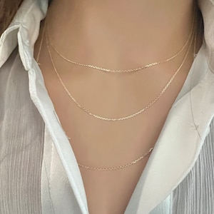 May include: Three gold chain necklaces layered on a person's neck. The chains are delicate and have a simple design.