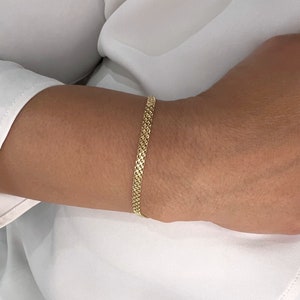 May include: A gold bracelet featuring a fine, intricate woven mesh chain design. The metal has a polished, reflective finish that catches the light, creating a textured appearance across the surface of the narrow, flexible link band.
