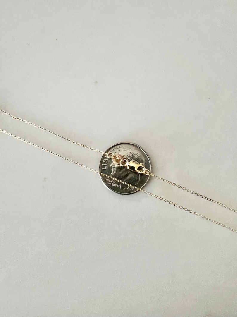 May include: Two gold chains laid out on a white surface, with a US quarter coin placed on top of the chains. The coin is dated 2021.