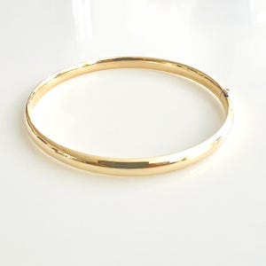 May include: A gold bangle bracelet with a smooth, polished surface. The bracelet is a simple, elegant design, perfect for everyday wear. The gold color is bright and reflective, adding a touch of luxury.