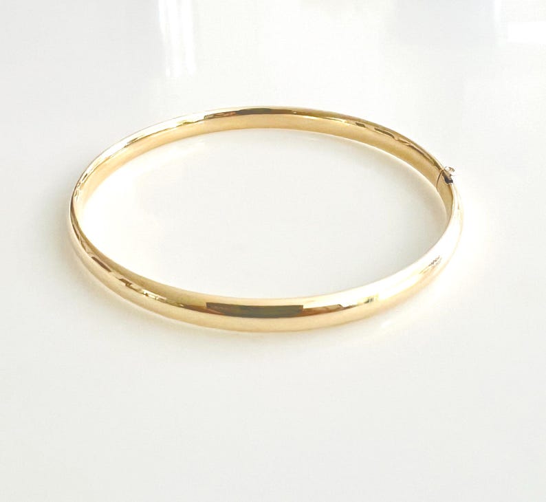 May include: A gold bangle bracelet with a smooth, polished surface. The bracelet is a simple, elegant design, perfect for everyday wear. The gold color is bright and reflective, adding a touch of luxury.