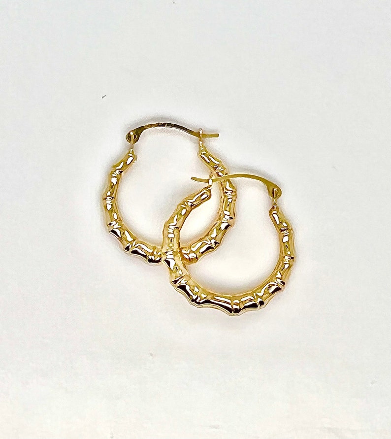 Puede incluir: Un par de pendientes de aro dorados con dise&ntilde;o de bamb&uacute;. Los pendientes tienen un acabado pulido y un cierre seguro. Los aros son de forma ovalada y se muestran sobre un fondo blanco.