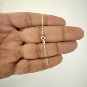 May include: A delicate gold chain necklace featuring a polished finish and a small, circular spring ring clasp. The chain consists of thin, interconnected oval links that create a smooth, continuous strand, showcasing a classic and refined design.