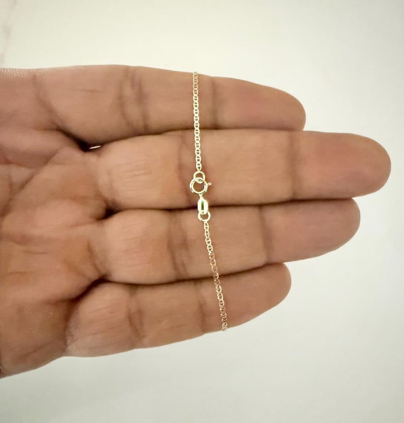 May include: A delicate gold chain necklace featuring a polished finish and a small, circular spring ring clasp. The chain consists of thin, interconnected oval links that create a smooth, continuous strand, showcasing a classic and refined design.