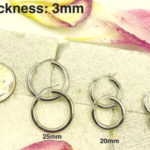 K&ouml;nnte beinhalten: Silberne Creolen in drei Gr&ouml;&szlig;en: 25 mm, 20 mm und 15 mm. Die Ohrringe werden neben einer M&uuml;nze zum Gr&ouml;&szlig;envergleich dargestellt. Die Dicke der Ohrringe betr&auml;gt 3 mm.