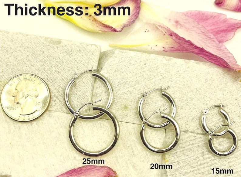 K&ouml;nnte beinhalten: Silberne Creolen in drei Gr&ouml;&szlig;en: 25 mm, 20 mm und 15 mm. Die Ohrringe werden neben einer M&uuml;nze zum Gr&ouml;&szlig;envergleich dargestellt. Die Dicke der Ohrringe betr&auml;gt 3 mm.