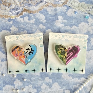 May include: Two heart-shaped acrylic pins with colourful skateboard designs. The left pin features a blue and orange skateboard with the text "MERMAID" on it. The right pin features a purple and green skateboard with a black and white design. Both pins have the text "Cloudy Aster" on the card they are displayed on.