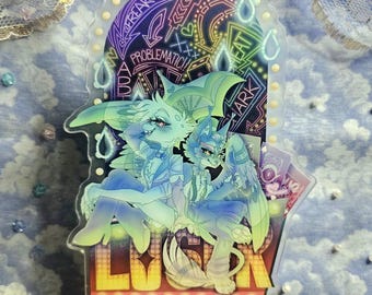 Puede incluir: Un soporte de acrílico transparente con un diseño de neón que presenta dos personajes de dibujos animados. Los personajes son una criatura azul y verde con alas y una criatura azul con una corona. El soporte tiene un letrero de neón que dice "LUCK" y las palabras "Problematic" y "Heat" son visibles en el fondo.