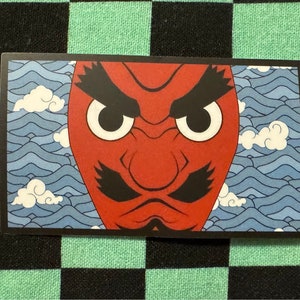 Peut inclure: Un masque de démon rouge avec des sourcils noirs, une moustache noire et des yeux noirs. Le masque est placé sur un fond de vagues bleues et blanches.