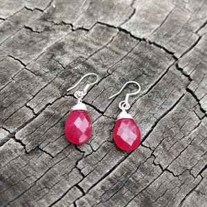 May include: A pair of silver earrings with pink gemstone drops. The earrings have a simple design and are perfect for everyday wear.