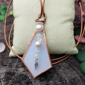 May include: A white glass pendant with a copper frame and a silver angel wing charm. The pendant is strung with white pearls and clear crystals on a copper wire.