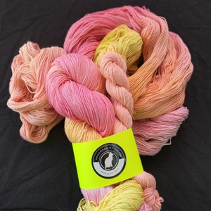 May include: A skein of hand-dyed yarn in shades of pink, orange, and yellow. The yarn is wrapped around a yellow label with the text "Handmade by Catkin" and a black cat silhouette.