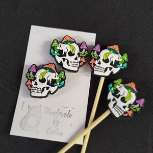 May include: Three black and white skull shaped drink stirrers with colourful mushroom designs. The stirrers are handmade by Catkin.