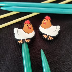 Op de afbeelding: Twee groene breinaalden met kippenvormige steekmarkeringen. De kippenvormige steekmarkierungen zijn wit met bruine koppen en rode kammen.