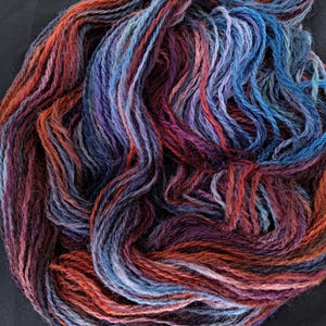 May include: Close-up of a skein of hand-dyed yarn. The yarn displays a mix of colours, including orange, red, blue, purple, and grey. The yarn is loosely arranged, highlighting its texture and colour variations. Suitable for knitting and crochet projects.