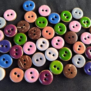 May include: A collection of round, two-hole buttons in a variety of colors including pink, blue, green, purple, white, and brown. Some buttons feature a smooth, glossy finish, while others display a natural, textured brown wood grain pattern.