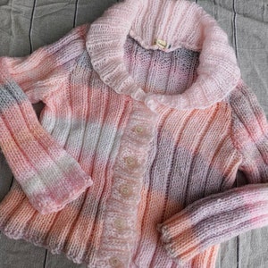 May include: A pink, white, and gray striped knitted cardigan with a ruffled collar and button closure.