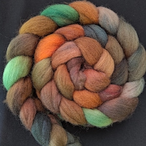 May include: A tightly coiled braid of colorful wool roving. The roving features a blend of earthy tones, including shades of green, orange, brown, and gray. The wool is soft and appears to be ideal for spinning or felting projects.