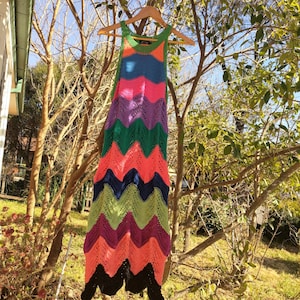 May include: A colorful crochet dress with a zig-zag pattern in shades of pink, green, blue, and purple. The dress is sleeveless and has a halter neckline.