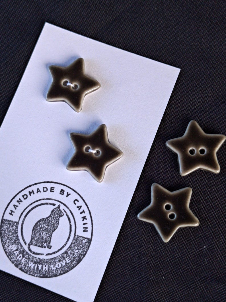 May include: Four star-shaped buttons with a dark brown and cream gradient finish, each featuring two center holes. Two buttons are attached to a white display card printed with a cat icon and the text HANDMADE BY CATKIN MADE WITH LOVE.