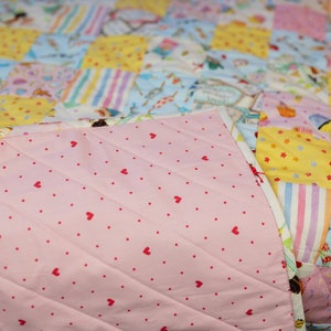 May include: A pink quilt with a white and pink striped pattern on one side and a pink fabric with red hearts on the other side.