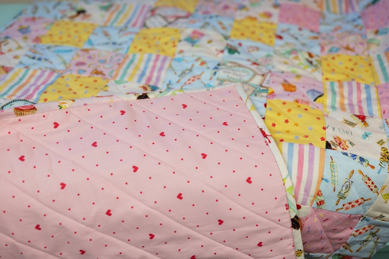 May include: A pink quilt with a white and pink striped pattern on one side and a pink fabric with red hearts on the other side.