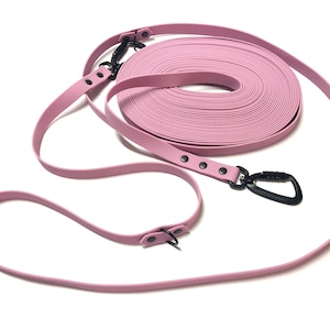 May include: A pale pink dog training lead with black metal fixings. The lead is coiled and features a black carabiner clip. The lead is made of a durable material and is designed for outdoor use.