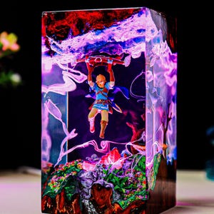 May include: A rectangular resin sculpture featuring a miniature figure of a character from a video game, suspended within a vibrant, colorful landscape. The sculpture has a mix of red, blue, and purple hues, with a detailed base.