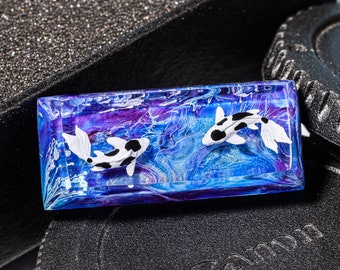 May include: A small rectangular resin paperweight with a blue, purple, and white marbled design. Two white and black koi fish are swimming in the resin.