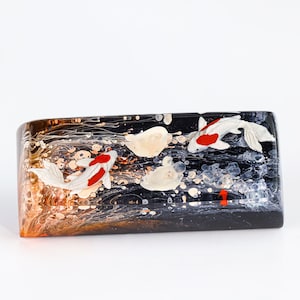 May include: A rectangular block of clear resin with a black and white swirling pattern. Three white koi fish with red accents are embedded in the resin.