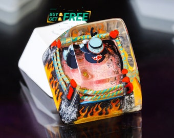 Pode incluir: Um keycap de resina com um design colorido que apresenta um personagem em um ringue de luta livre com chamas e cordas. O keycap é transparente e mostra a estrutura interna. O texto "BUY GET FREE" é visível no fundo.
