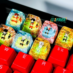 Könnte beinhalten: Sieben bunte Keycaps mit verschiedenen Comicfiguren auf einer roten Tastatur. Die Keycaps sind durchsichtig und haben eine glänzende Oberfläche. Die Tastatur hat die Buchstaben W, E, R, T, S, D, 5% und 6 auf den Tasten.