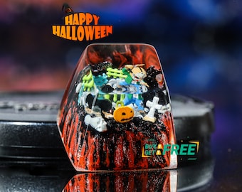 Pode incluir: Uma tecla de resina transparente com tema de Halloween. A tecla está cheia de pequenas figuras com tema de Halloween, incluindo uma abóbora, um fantasma, uma bruxa e um esqueleto. A tecla também é decorada com tinta preta e vermelha, dando-lhe um visual assustador. O texto "BUY 1 GET 1 FREE" está impresso na tecla.