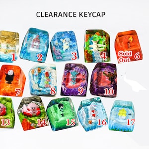 Può includere: Una collezione di tasti per tastiera in resina colorata con vari disegni, tra cui personaggi dei cartoni animati e scene acquatiche. I tasti sono numerati ed etichettati "CLEARANCE KEYCAP". Un tasto è contrassegnato come "Sold Out".