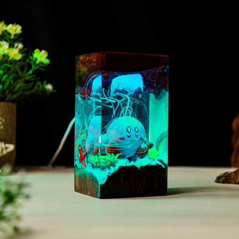 May include: A rectangular resin night light featuring a cartoon character in a glowing blue and green underwater scene. The wooden base has a dark brown color, and the light emits a soft glow.
