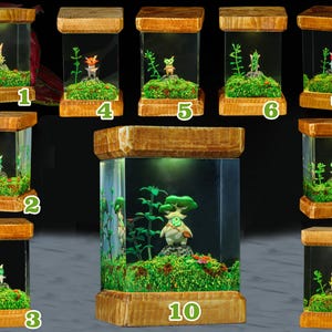 K&ouml;nnte beinhalten: Zehn kleine Holzterrarien mit Glasseiten, jedes mit einer Miniaturfigur und Gr&uuml;npflanzen. Die Terrarien sind von innen beleuchtet und strahlen ein warmes Licht aus. Die Figuren sind alle unterschiedlich, aber sie haben alle einen &auml;hnlichen Stil und sind aus einem hellen Material gefertigt. Die Terrarien sind von 1 bis 10 nummeriert.