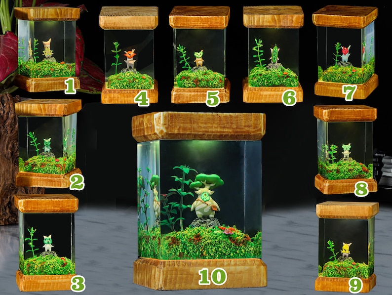 K&ouml;nnte beinhalten: Zehn kleine Holzterrarien mit Glasseiten, jedes mit einer Miniaturfigur und Gr&uuml;npflanzen. Die Terrarien sind von innen beleuchtet und strahlen ein warmes Licht aus. Die Figuren sind alle unterschiedlich, aber sie haben alle einen &auml;hnlichen Stil und sind aus einem hellen Material gefertigt. Die Terrarien sind von 1 bis 10 nummeriert.