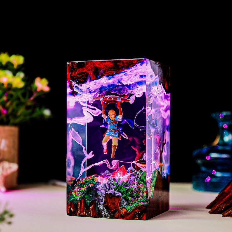 May include: A rectangular resin sculpture featuring a miniature figure of a character from a video game, suspended within a vibrant, colorful landscape. The sculpture has a mix of red, blue, and purple hues, with a detailed base.