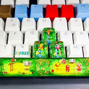 May include: A green and yellow keyboard keycap set featuring Winnie the Pooh and friends. The keycaps are made of resin and have a translucent finish. The keycaps are arranged in a row on a white keyboard. The keycaps are labeled with the letters 'T', 'V', 'G', 'J', 'K', and 'M'. The keycaps are surrounded by other keyboard keys, including the keys 'E', 'R', 'O', 'Y', 'U', 'F', and 'BUY GET A FREE'.