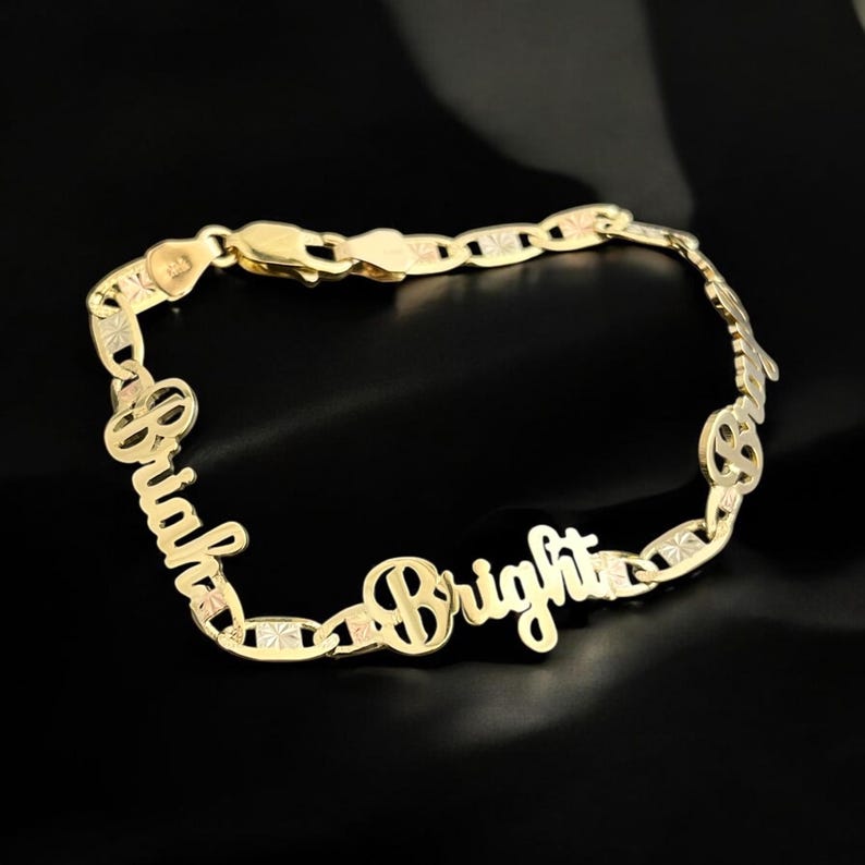 May include: A gold-colored bracelet with the names "Briah" and "Bright" in a cursive font. The bracelet has a chain link design with decorative accents. The background is black.