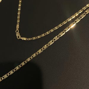 May include: A gold chain necklace with a mariner link design. The chain is made of solid gold and has a polished finish.