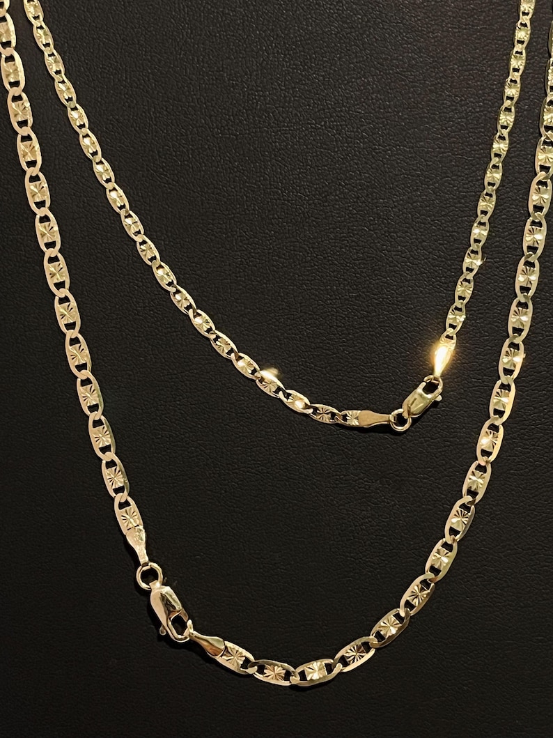 May include: A gold chain necklace with a mariner link design. The chain has a diamond-cut finish and is made of 14k gold.