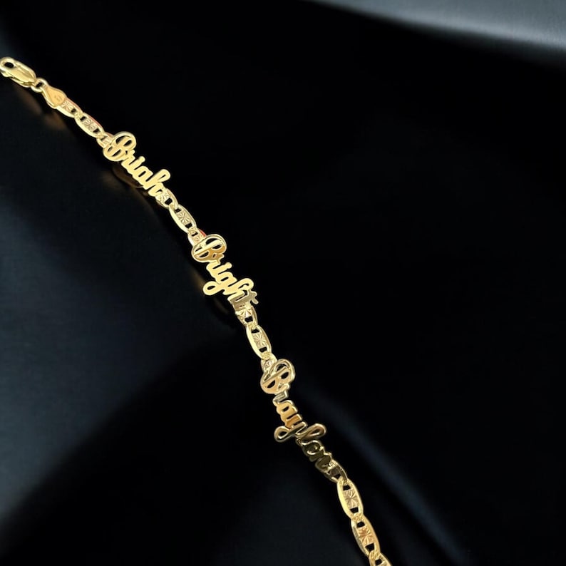 May include: A gold-colored bracelet with the words "Bright" and "Braylove" spelled out in a cursive font. The bracelet is made of linked chain segments and is displayed against a black background.