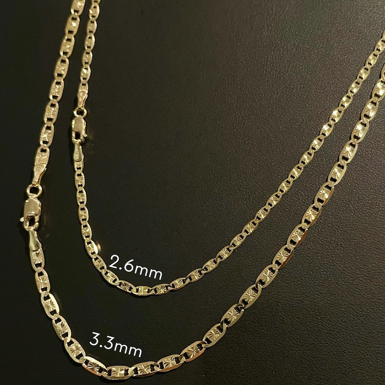 May include: Two gold chains with a mariner link pattern. The chain on the top is 2.6 mm wide and the chain on the bottom is 3.3 mm wide.