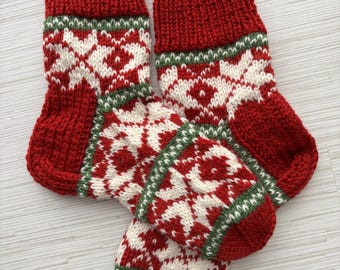 May include: Two red and white knitted Christmas stockings with a traditional Nordic pattern. The stockings have a red cuff, a white and red patterned body, and a green border. The stockings are made of a thick, textured yarn.