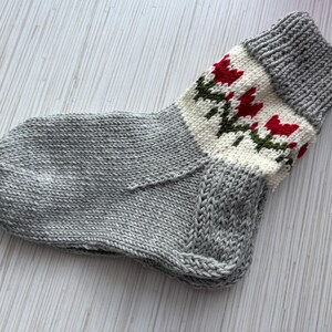May include: A gray knitted sock with a white and red floral pattern around the top.