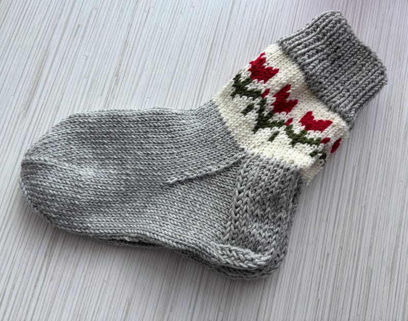 May include: A gray knitted sock with a white and red floral pattern around the top.
