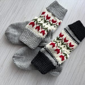 May include: A pair of gray and white knitted socks with a red and green floral pattern. The socks are made of a soft, comfortable material and are perfect for keeping your feet warm in the winter.