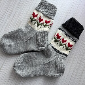 May include: Two pairs of gray knitted socks with white and red tulip designs. The socks have a black cuff on one pair.